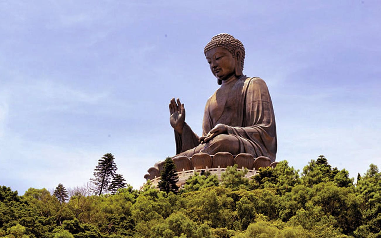 Tian Tan Buddha statue at Ngong Ping, Hong Kong, surrounded by lush greenery.