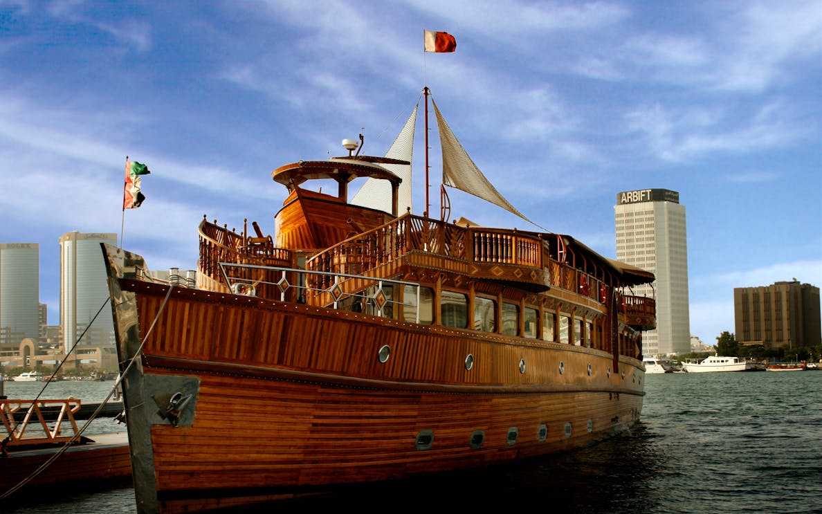 Traditional wooden dhow on Dubai Creek with city skyline in the background.