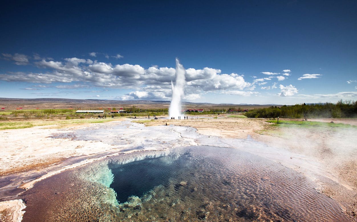 Geyser erupting in Iceland's Golden Circle with hot spring in foreground.