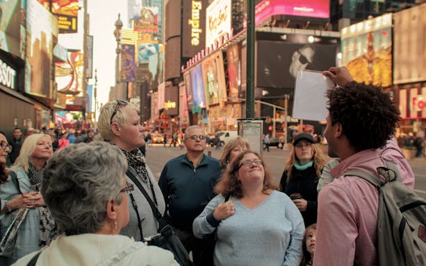 Tour group in Times Square, New York City, learning about Disney on Broadway with a guide.