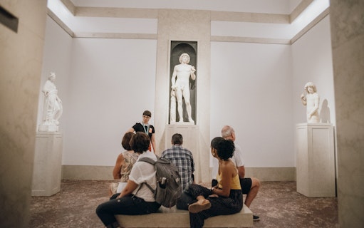 Tour group at Metropolitan Museum of Art viewing classical sculptures.