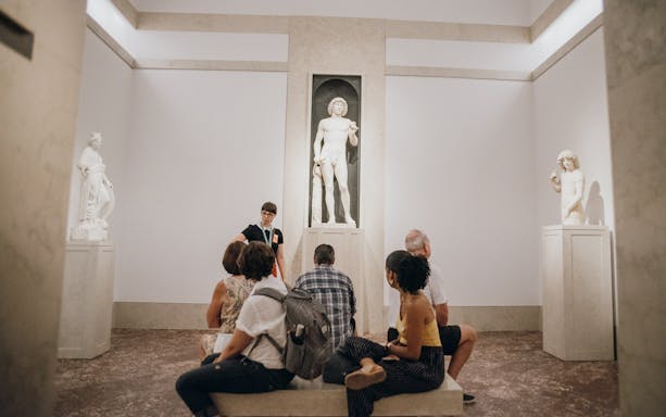 Tour group at Metropolitan Museum of Art viewing classical sculptures.