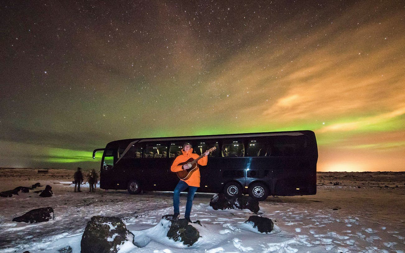Bus tour under Northern Lights near Reykjavik with musician playing guitar.