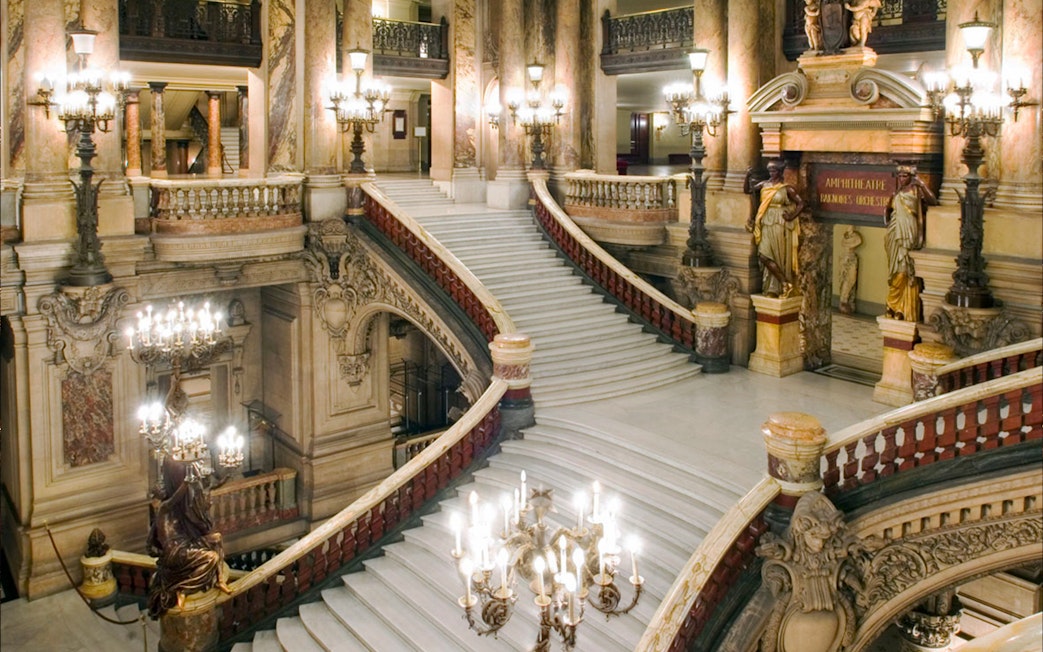 Grand staircase inside Opera Garnier, Paris, with ornate architecture and chandeliers.