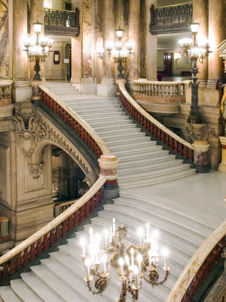 Grand staircase inside Opera Garnier, Paris, with ornate architecture and chandeliers.