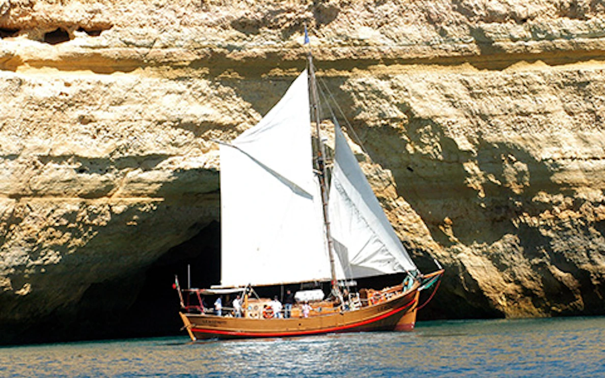 Sailing boat near Algarve cliffs during a cruising experience.