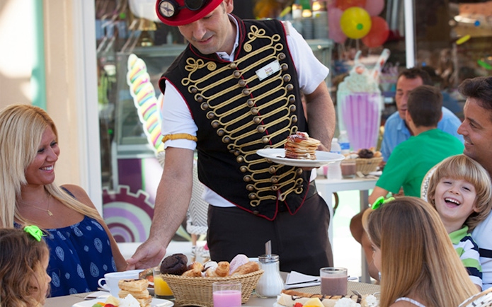 Server in themed attire serving food to a family at Katmandu Park.
