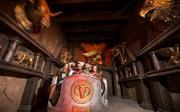 Visitors on a themed ride at Terra Mitica, surrounded by mythological statues.