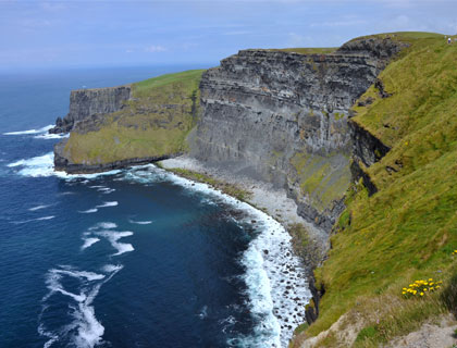 Cliffs of Moher coastline with ocean waves and grassy cliffs in Ireland.