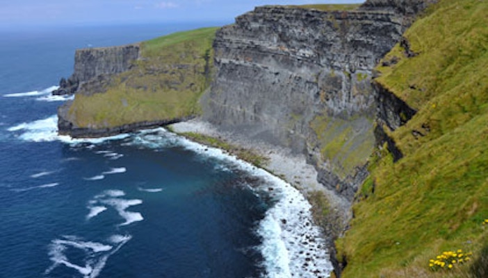 Cliffs of Moher coastline with ocean waves and grassy cliffs in Ireland.