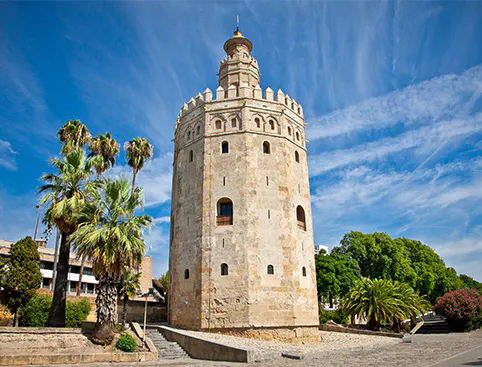 Torre del Oro in Seville with palm trees and blue sky.