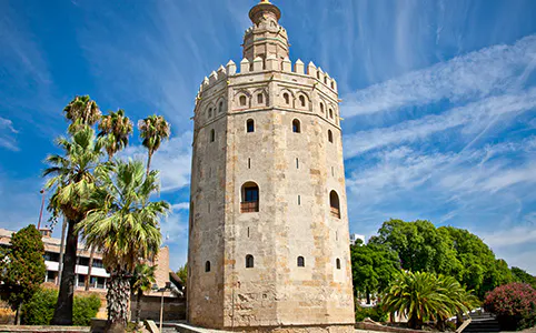 Torre del Oro in Seville with palm trees and blue sky.