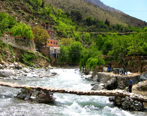 Ourika Valley river with footbridge and hillside village in Morocco.