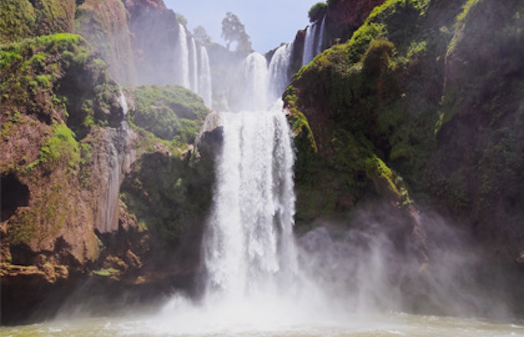 Ouzoud Falls cascading into a misty pool, surrounded by lush greenery.