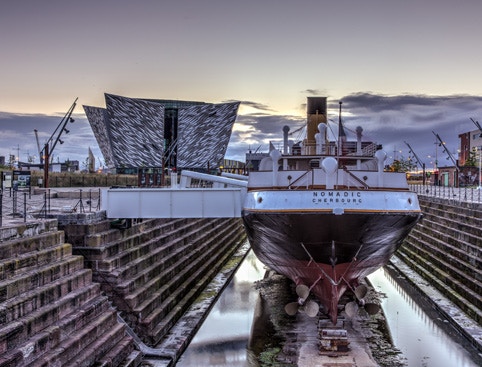 Titanic Belfast museum and SS Nomadic ship in dry dock at sunset.