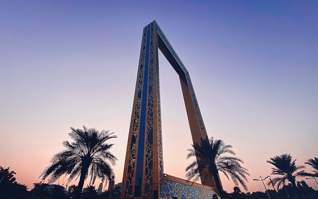 Dubai Frame at sunset with palm trees in the foreground.