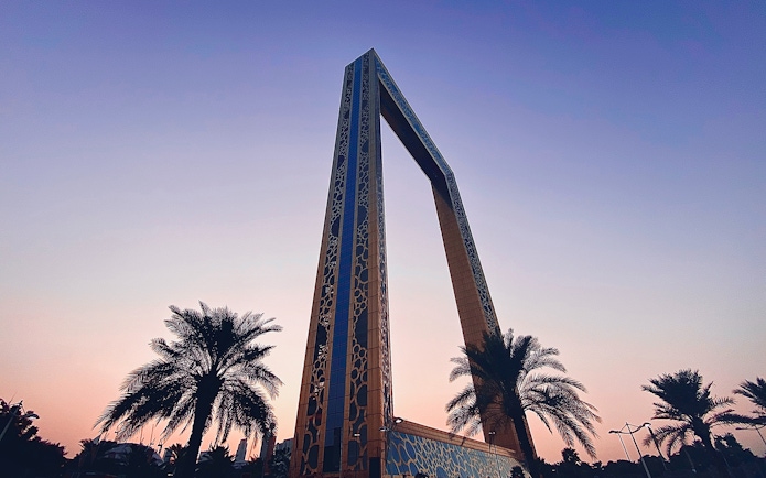 Dubai Frame at sunset with palm trees in the foreground.