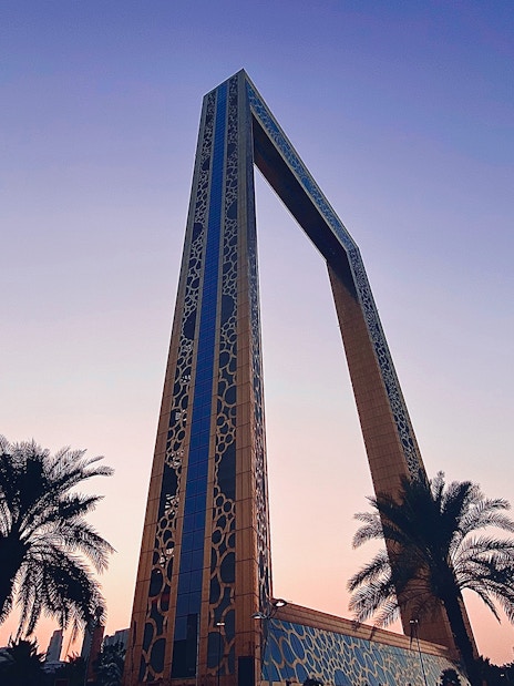 Dubai Frame at sunset with palm trees in the foreground.