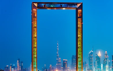 Dubai Frame with city skyline at night, highlighting IMG Worlds of Adventure tour.