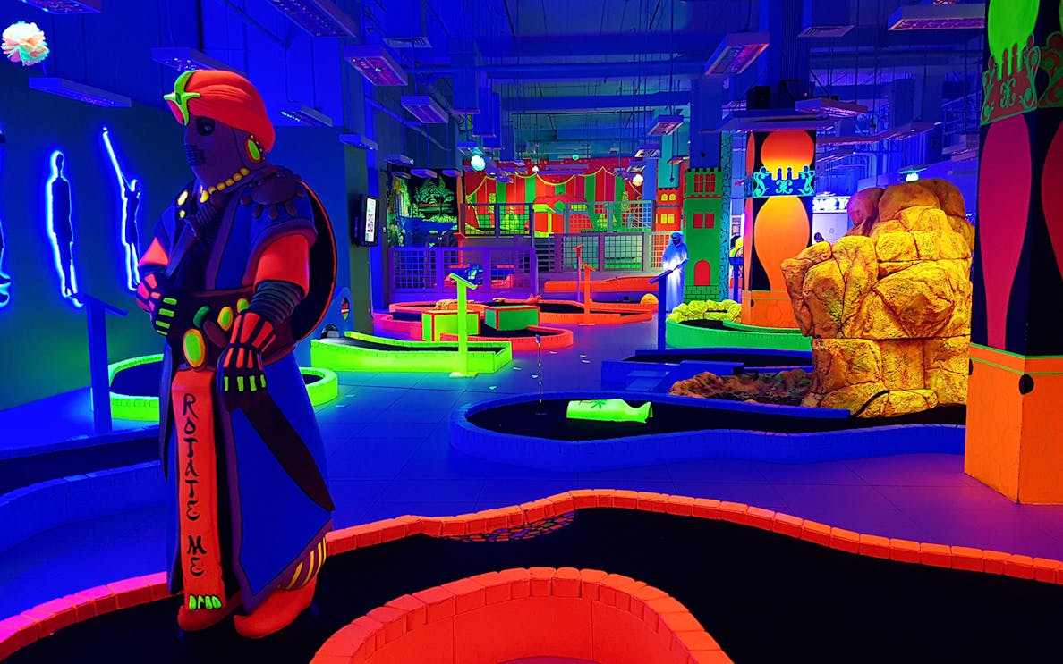 Glow in the dark mini golf course with neon obstacles and vibrant decor.