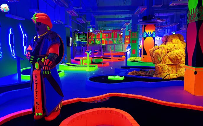 Glow in the dark mini golf course with neon obstacles and vibrant decor.