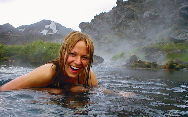Person enjoying Secret Lagoon hot spring with misty mountains in the background, Iceland.