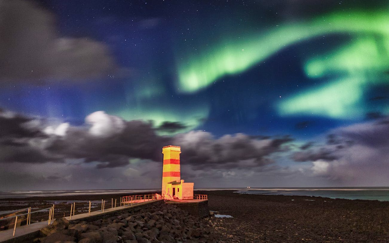 Northern Lights over a coastal lighthouse near Secret Lagoon Bath, Iceland.