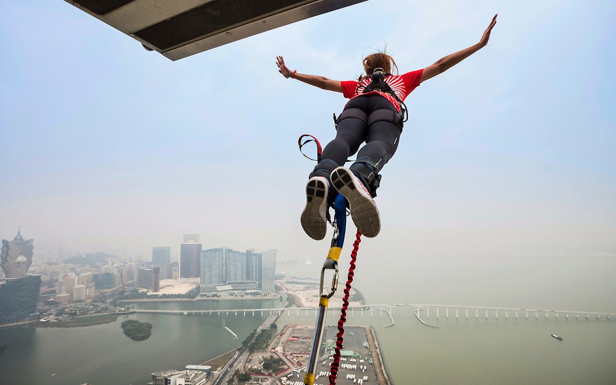 Bungee jumper leaping from AJ Hackett Sentosa platform with cityscape view.