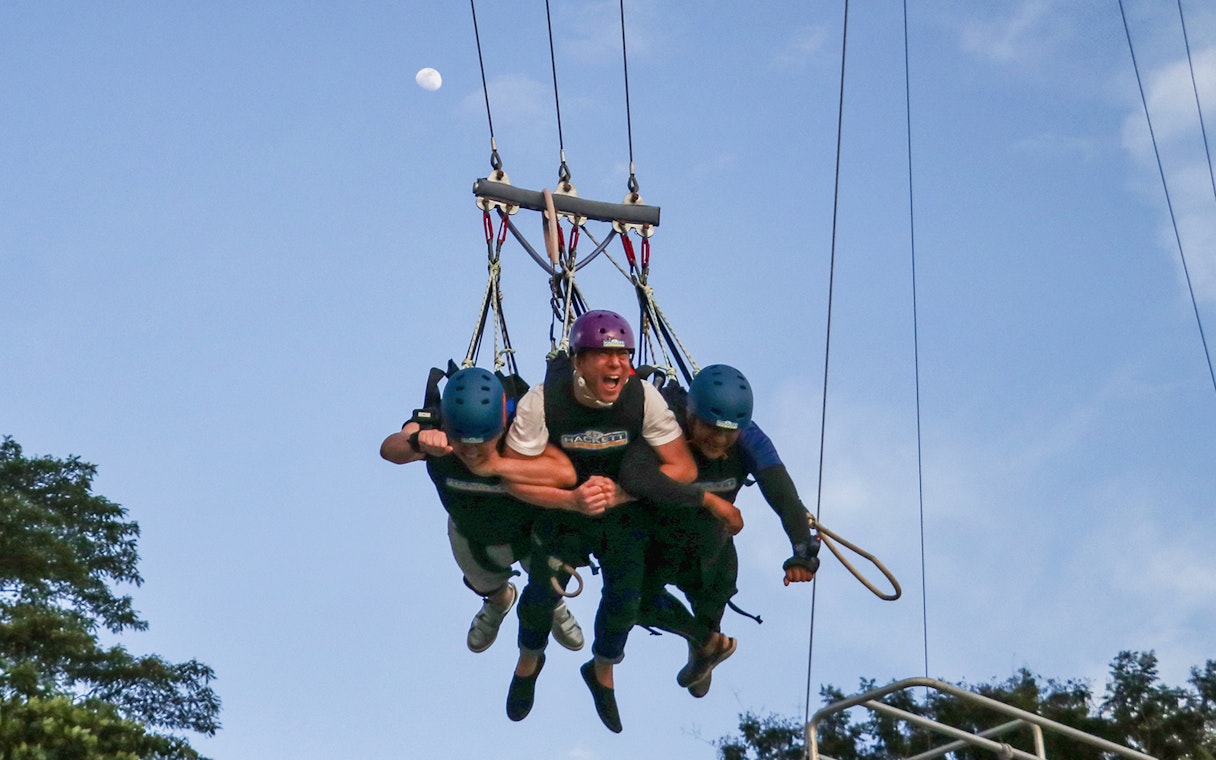 Three people in harnesses swinging at AJ Hackett Sentosa, Singapore.