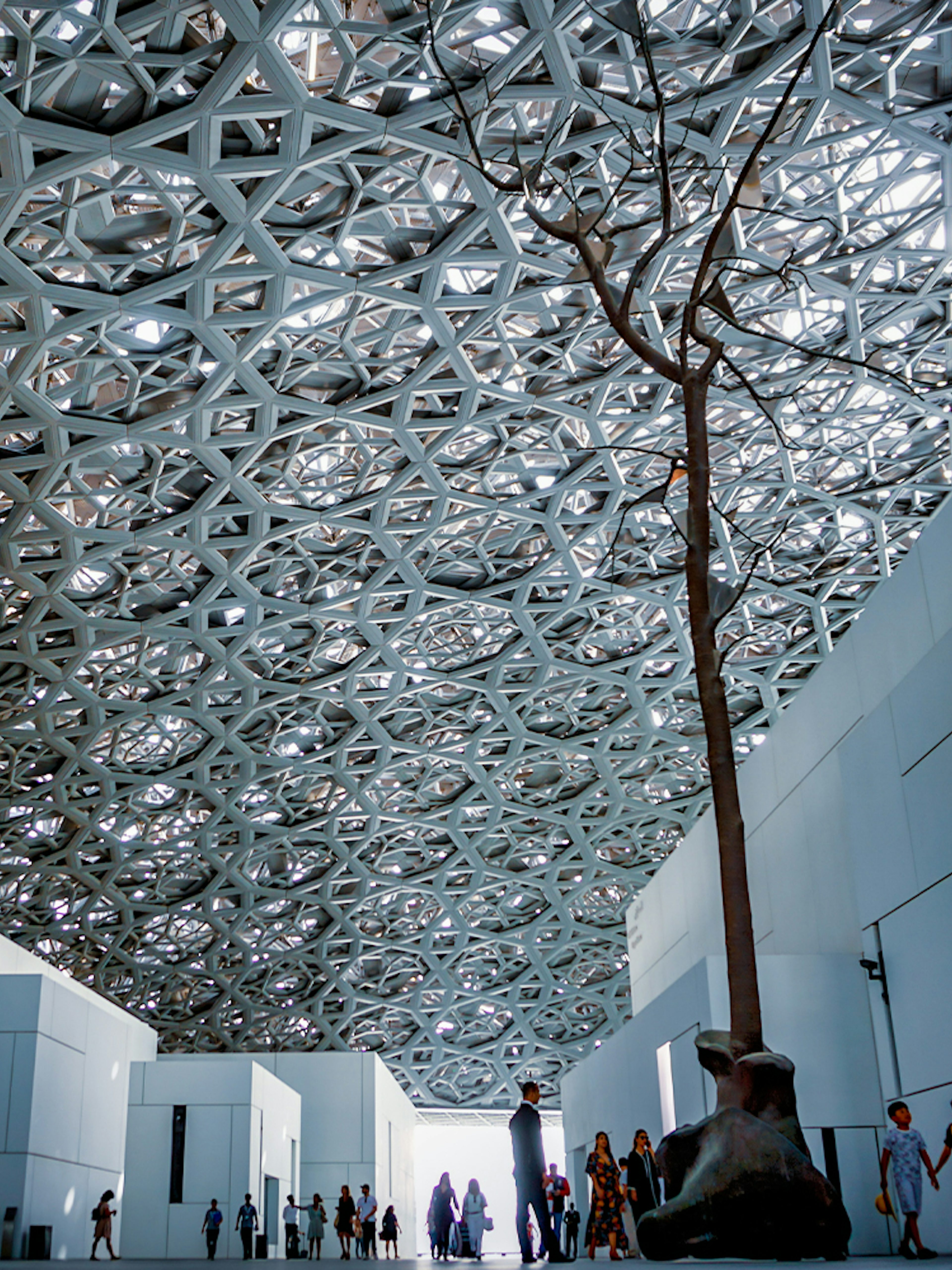 Louvre Abu Dhabi interior with geometric ceiling and visitors exploring.