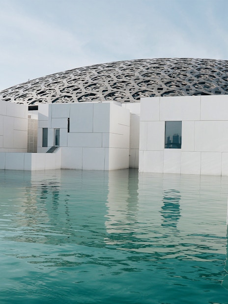 Louvre Abu Dhabi exterior with water reflection and dome structure.