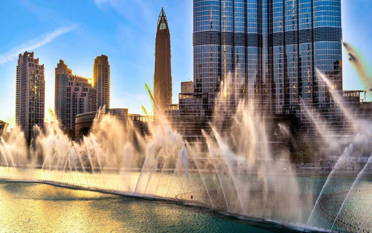 Burj Khalifa and Dubai Fountain Boardwalk with water jets at sunset.