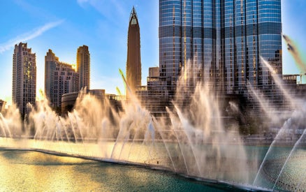 Burj Khalifa and Dubai Fountain Boardwalk with water jets at sunset.