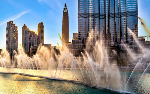Burj Khalifa and Dubai Fountain Boardwalk with water jets at sunset.
