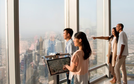 Visitors enjoying the view from Burj Khalifa observation deck, overlooking Dubai skyline.