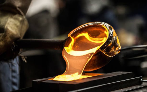 Glassblowing process with molten glass being shaped in a workshop.