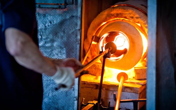 Glassblower shaping molten glass in a furnace during a glassblowing tour.