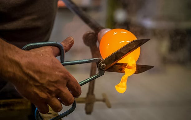 Glassblower shaping molten glass with tools during a workshop.