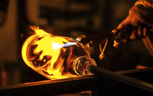 Glassblower shaping molten glass with a rod, showcasing the magical art of glassblowing.