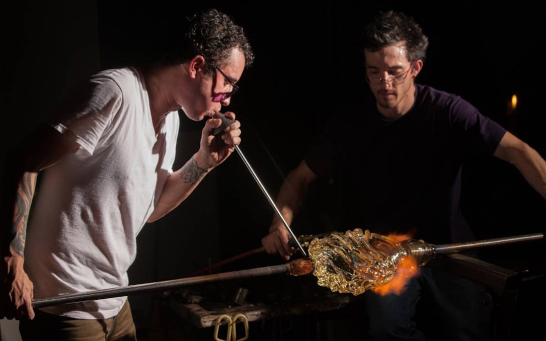 Glassblowers shaping molten glass with a blowpipe during a glassblowing demonstration.