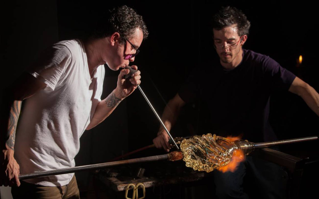 Glassblowers shaping molten glass with a blowpipe during a glassblowing demonstration.