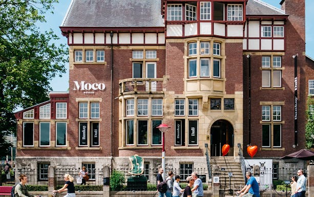 Moco Museum entrance in Amsterdam with people walking and cycling nearby.