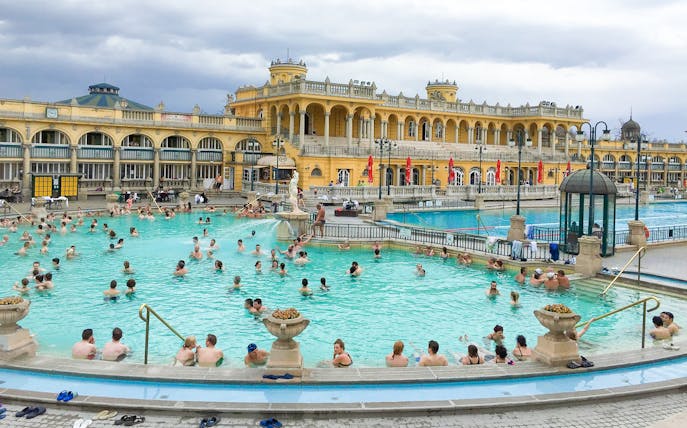 Visitors enjoying thermal pools at Széchenyi Spa, Budapest, with historic architecture in the background.