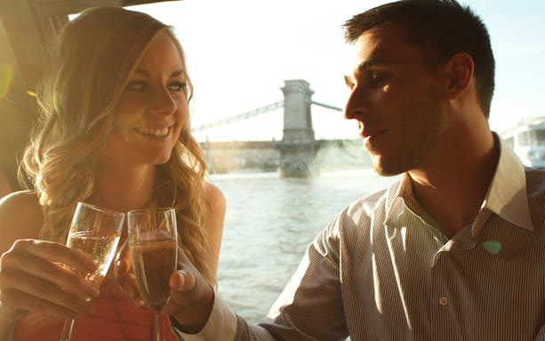 Couple toasting with champagne on Budapest Danube cruise, Chain Bridge in background.