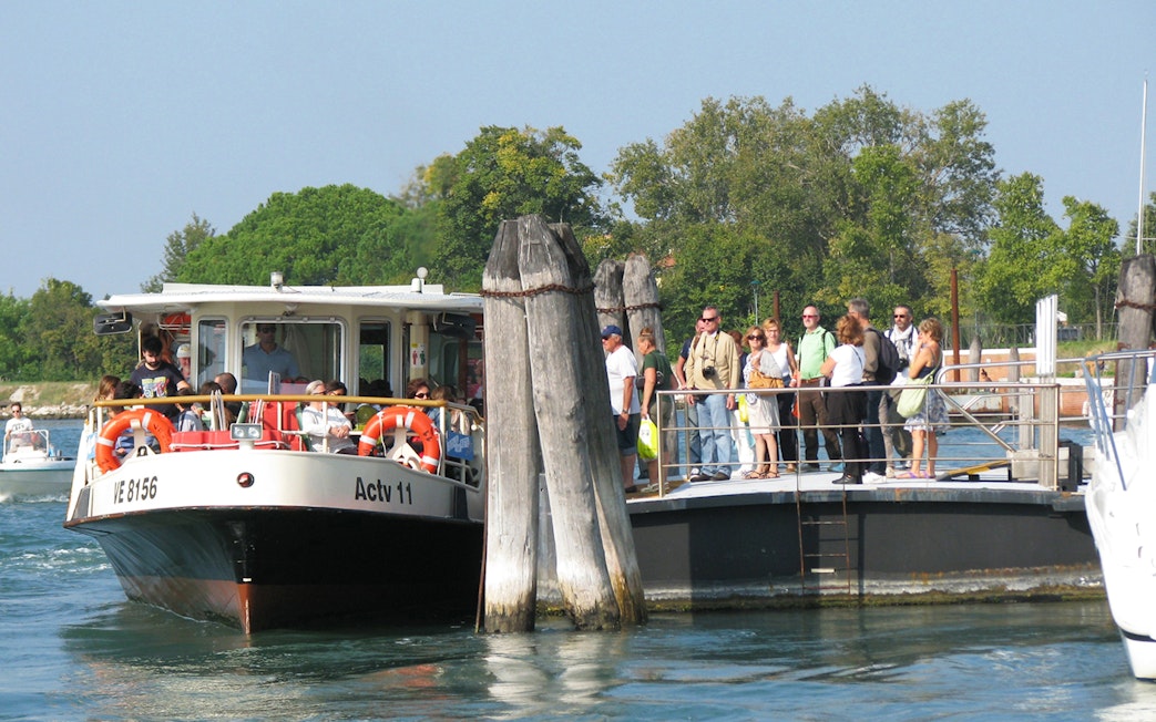 Venice ACTV water bus at dock with passengers boarding, surrounded by water and greenery.