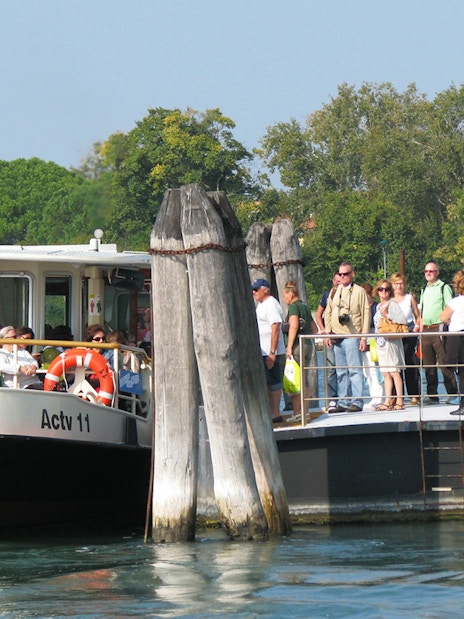 Venice ACTV water bus at dock with passengers boarding, surrounded by water and greenery.