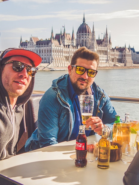 Group enjoying drinks on a Danube River cruise with Budapest Parliament in the background.