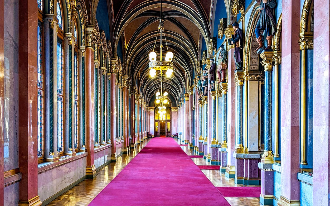 Interior hallway of the Hungarian Parliament with ornate arches and red carpet.