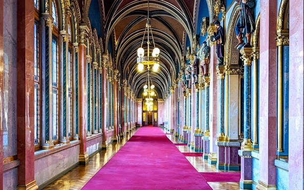 Interior hallway of the Hungarian Parliament with ornate arches and red carpet.