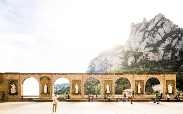 Montserrat Monastery courtyard with statues and mountain backdrop, part of self-guided tour from Barcelona.